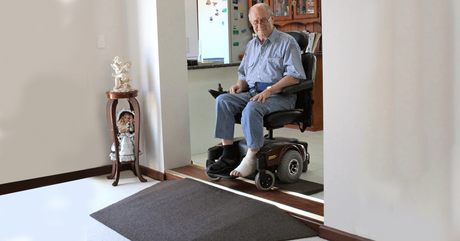 old man in a powered wheelchair approaching a doorway with a rubber threshold ramp