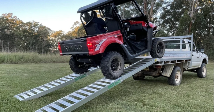Kymco UTV vehicle drive up aluminium ramps onto a white ute in a field