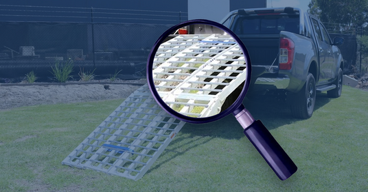 A truck ramp on grass, with a magnifying glass zooming in on the ramp's grid pattern, highlighting its detailed construction.