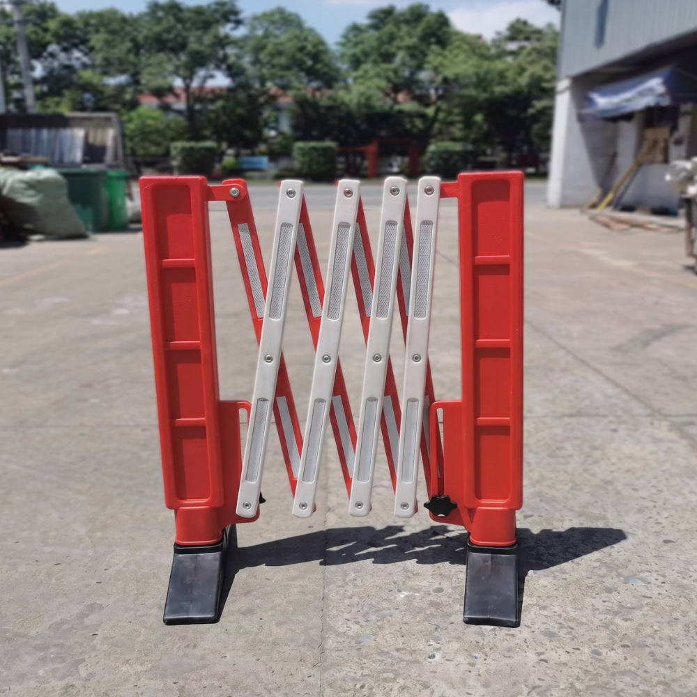 Red and white folding barrier on a concrete surface with trees and buildings in the background