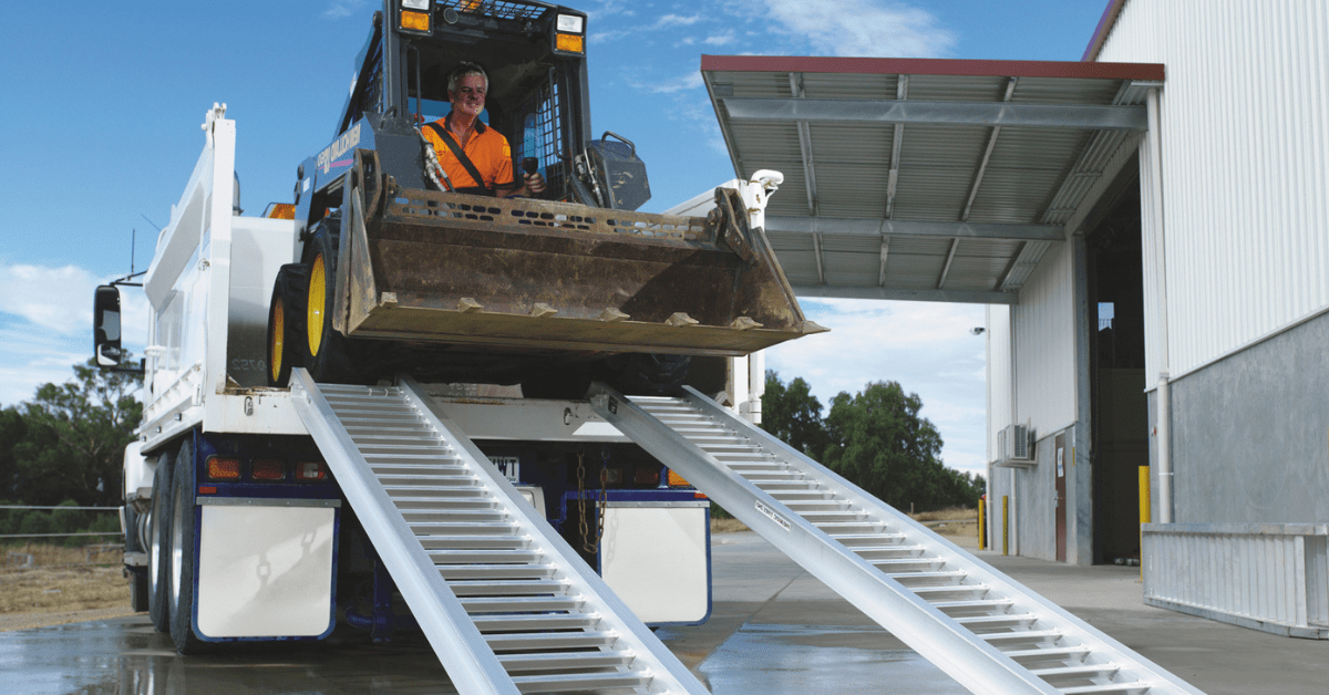 Skid steer loader front view in truck descending aluminium ramps