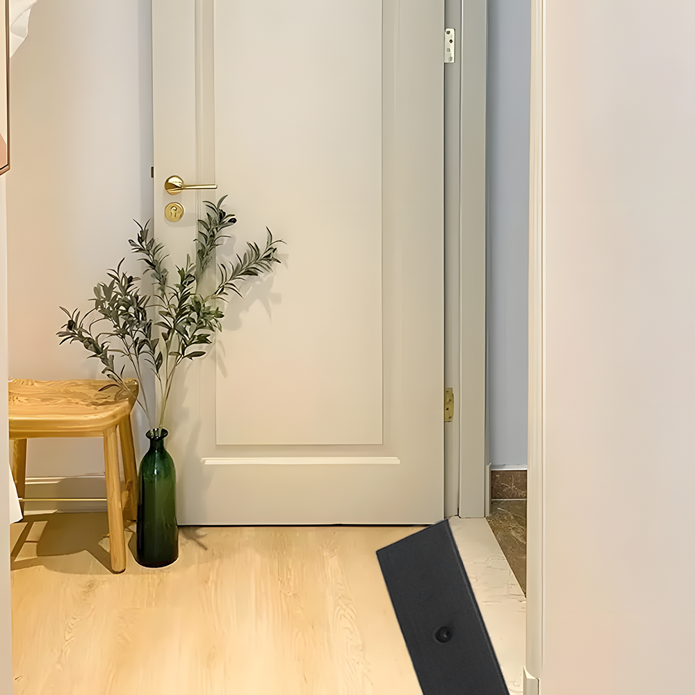 Ramp installed at an interior doorway, beside a wooden stool and a green vase with branches, against a closed white door.