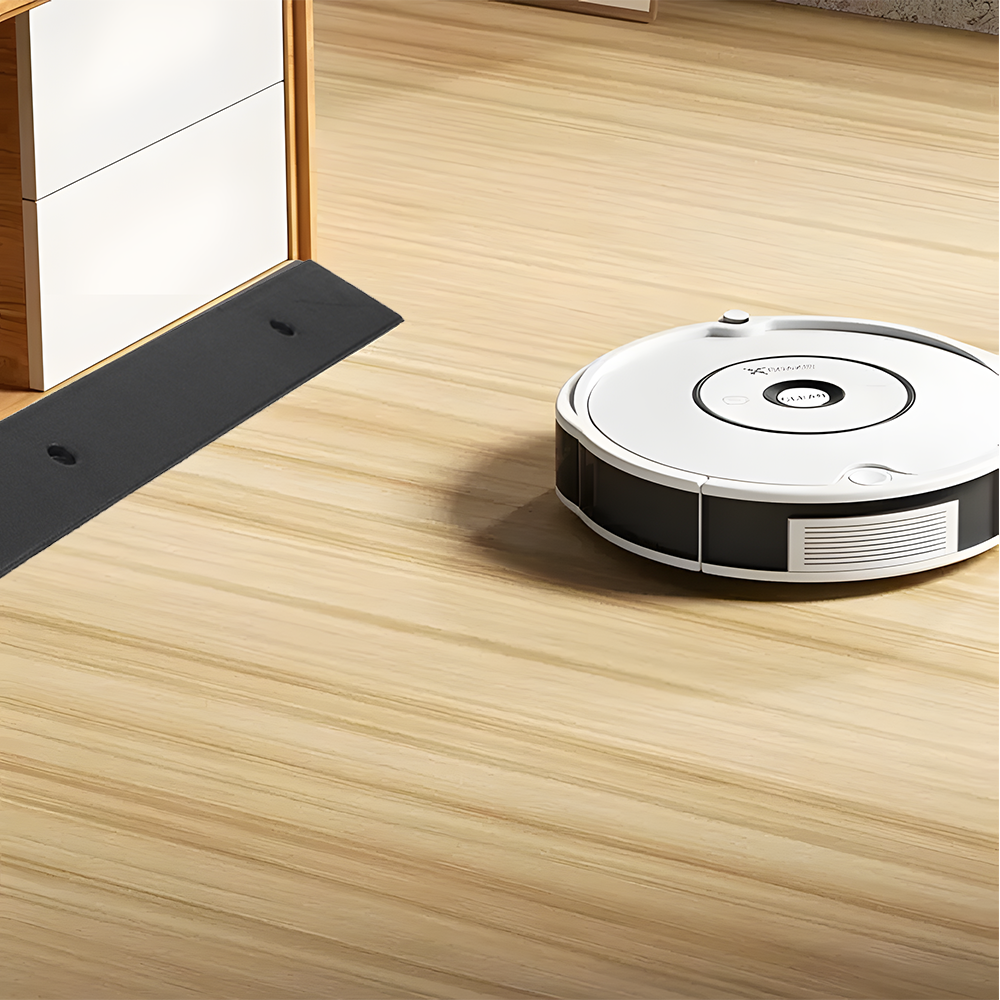 Robot vacuum approaching the rubber threshold ramp on light wooden flooring.