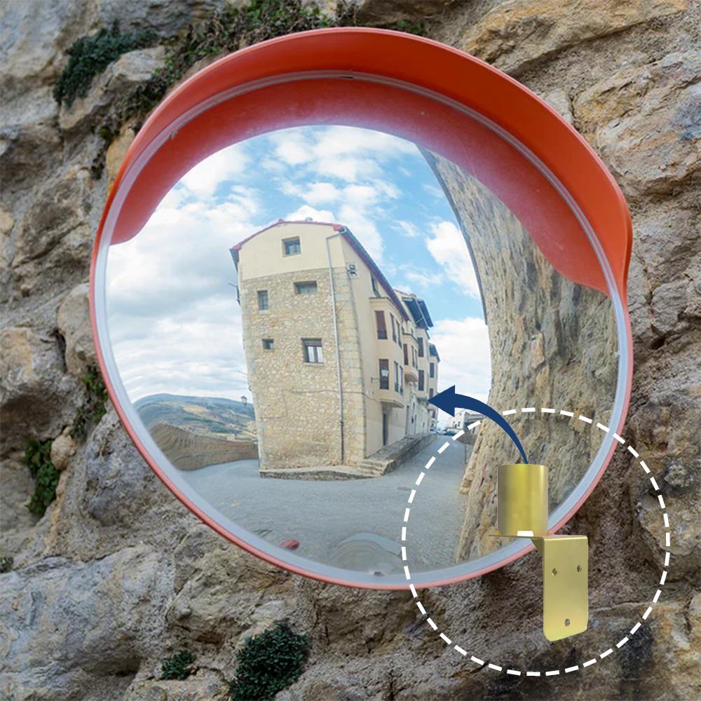 A round convex traffic mirror mounted on a rough stone wall, reflecting a narrow street with historic buildings. A dashed circle highlights the gold-coloured wall mount bracket, indicating its role in secure installation.
