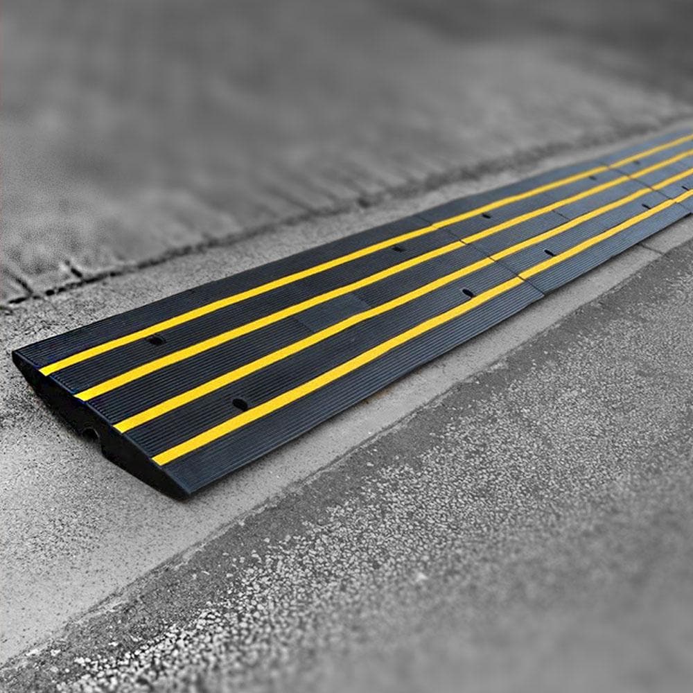 Close-up angle of modular black and yellow driveway kerb ramps installed on a rolled-edge kerb, showing interlocking sections and drainage gaps.