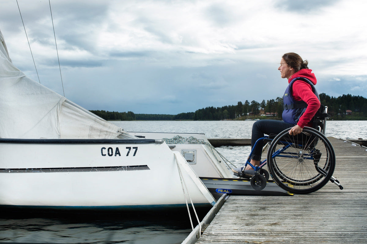 FEAL iRamp folding aluminium wheelchair ramp in use, wheelchair rolling from a jetty onto a boat