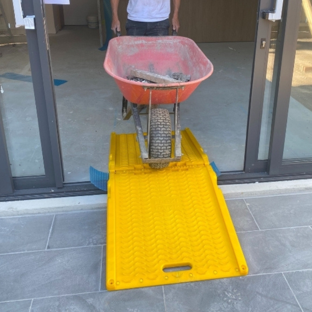 Yellow ramp placed at a door threshold with a wheelbarrow nearby.