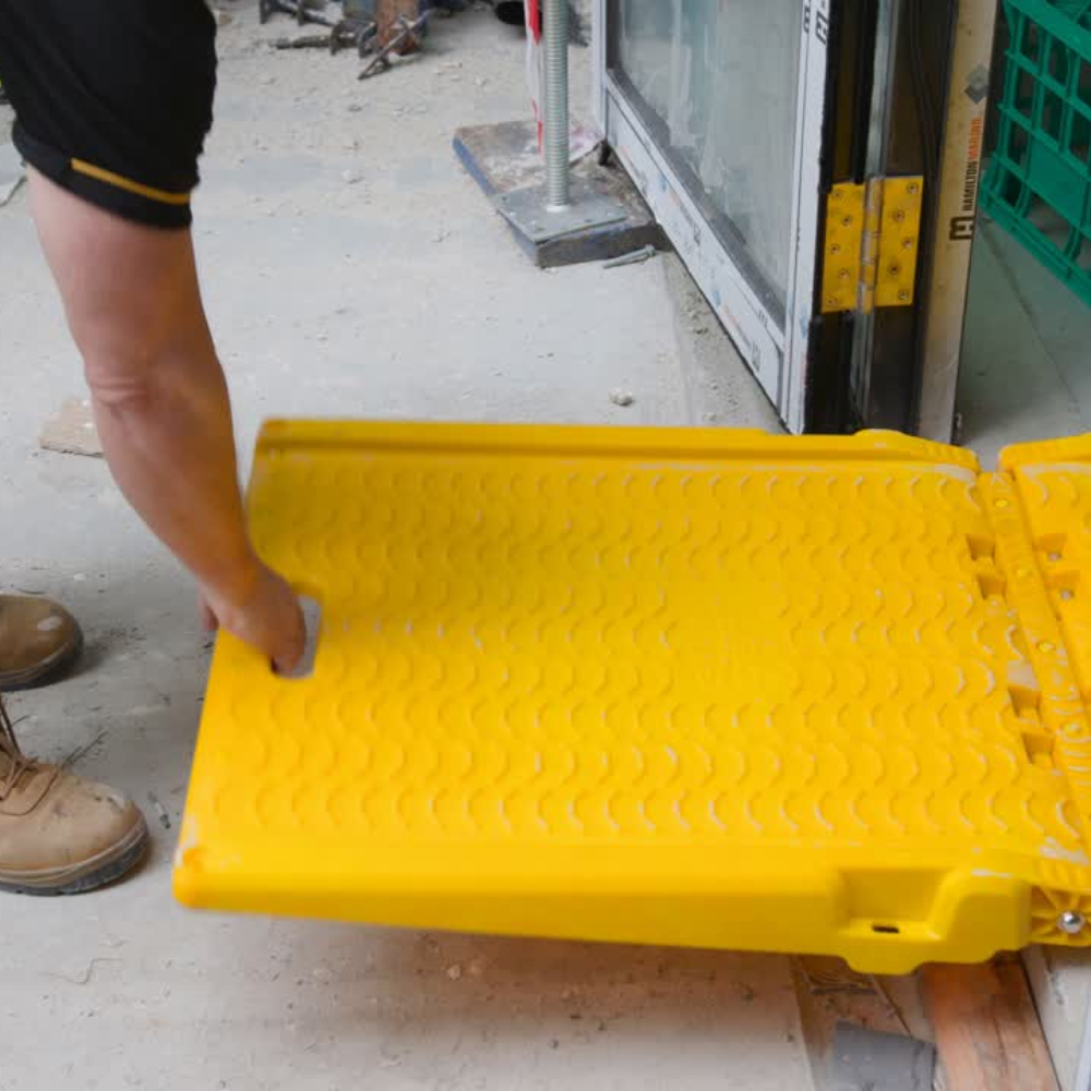 Person unfolding a yellow plastic ramp on a construction site.