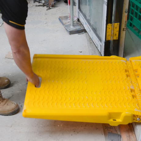 Person unfolding a yellow plastic ramp on a construction site.
