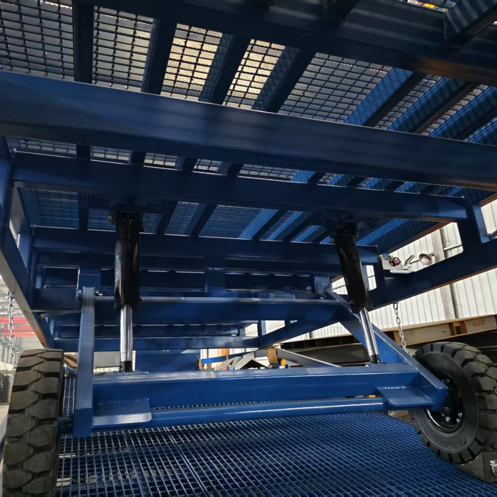 A close-up view of a large blue industrial trailer or cargo carrier frame with metal grates, hydraulic cylinders, and a black tire, photographed in a warehouse setting.