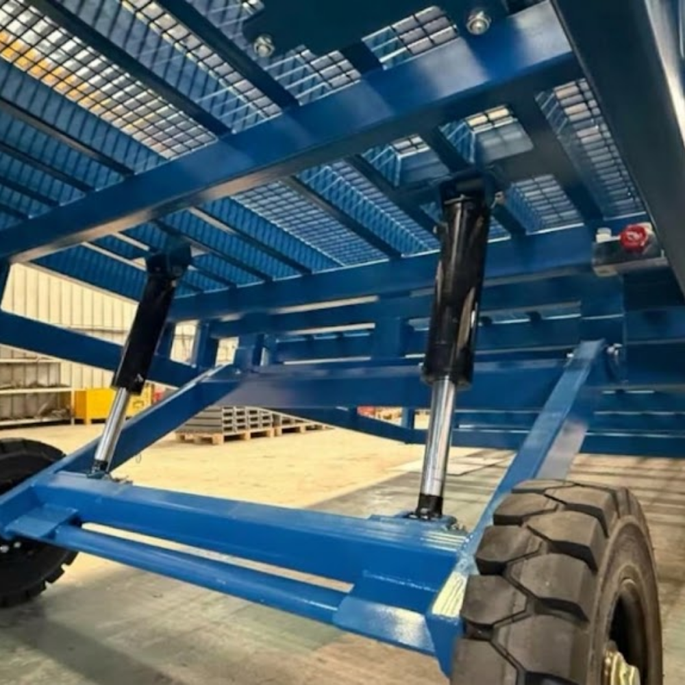 Close-up of a blue forklift yard ramp frame with black shock absorbers and a large treaded tire in an industrial warehouse setting.
