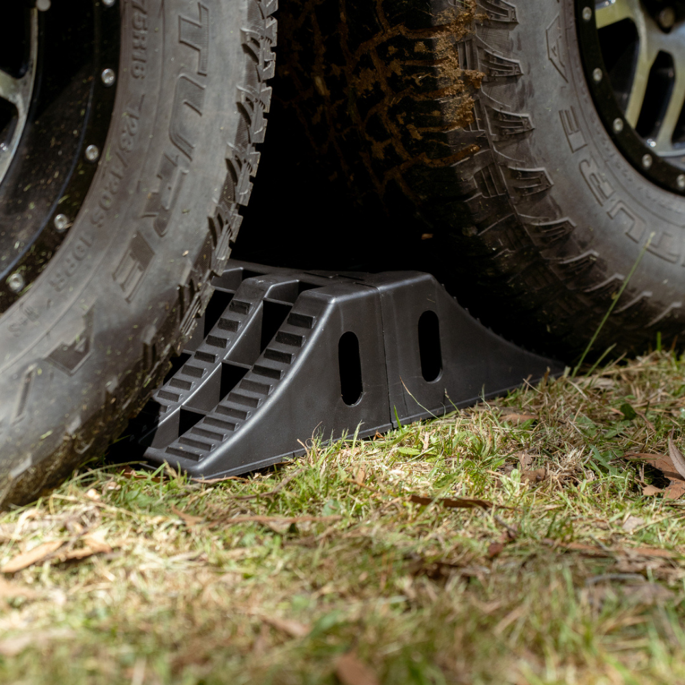 Black tire jack under two large tires on grass