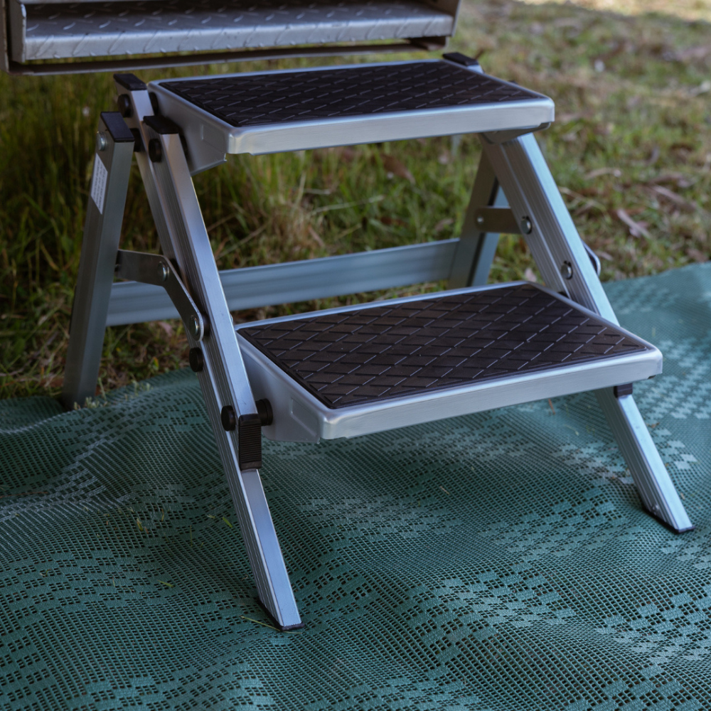 Two-step metal step stool on a green mat with grass in the background