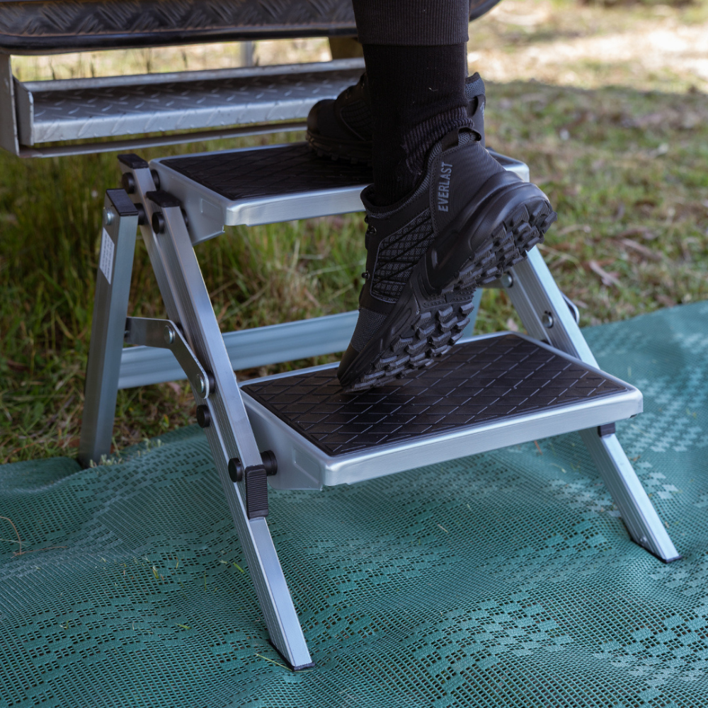 Person using a step stool outdoors on a green mat