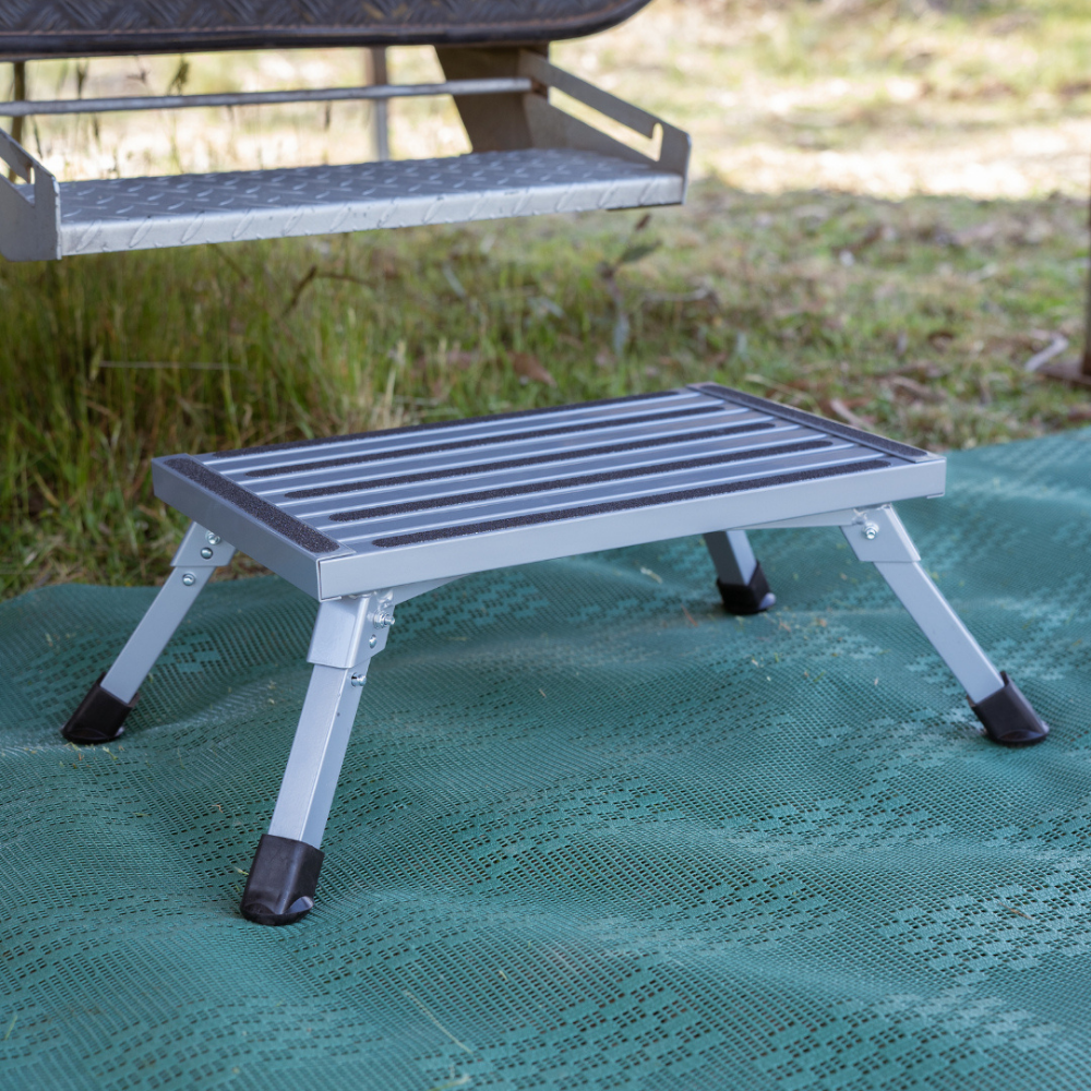Foldable step stool on a green mat with grass in the background