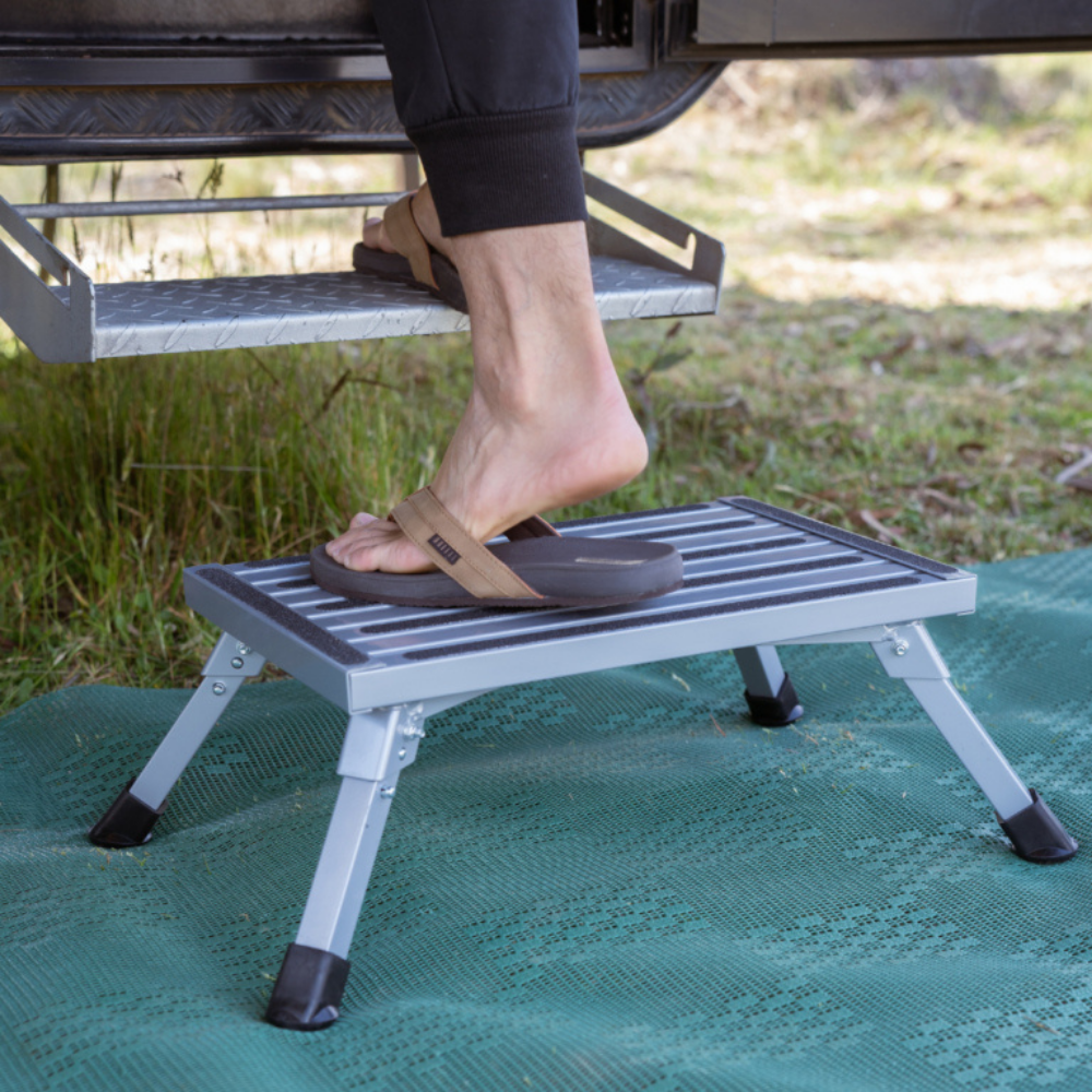 Person using a portable step stool outdoors on a grassy area