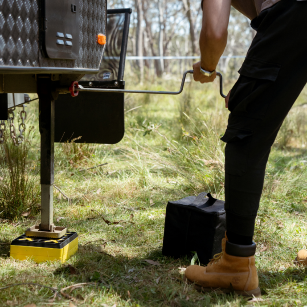 Person using a jack to lift a caravan on a grassy area