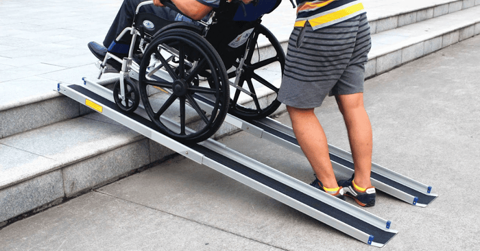 Two telescopic wheelchair ramps against concrete steps with a person in a wheelchair being pushed by another person