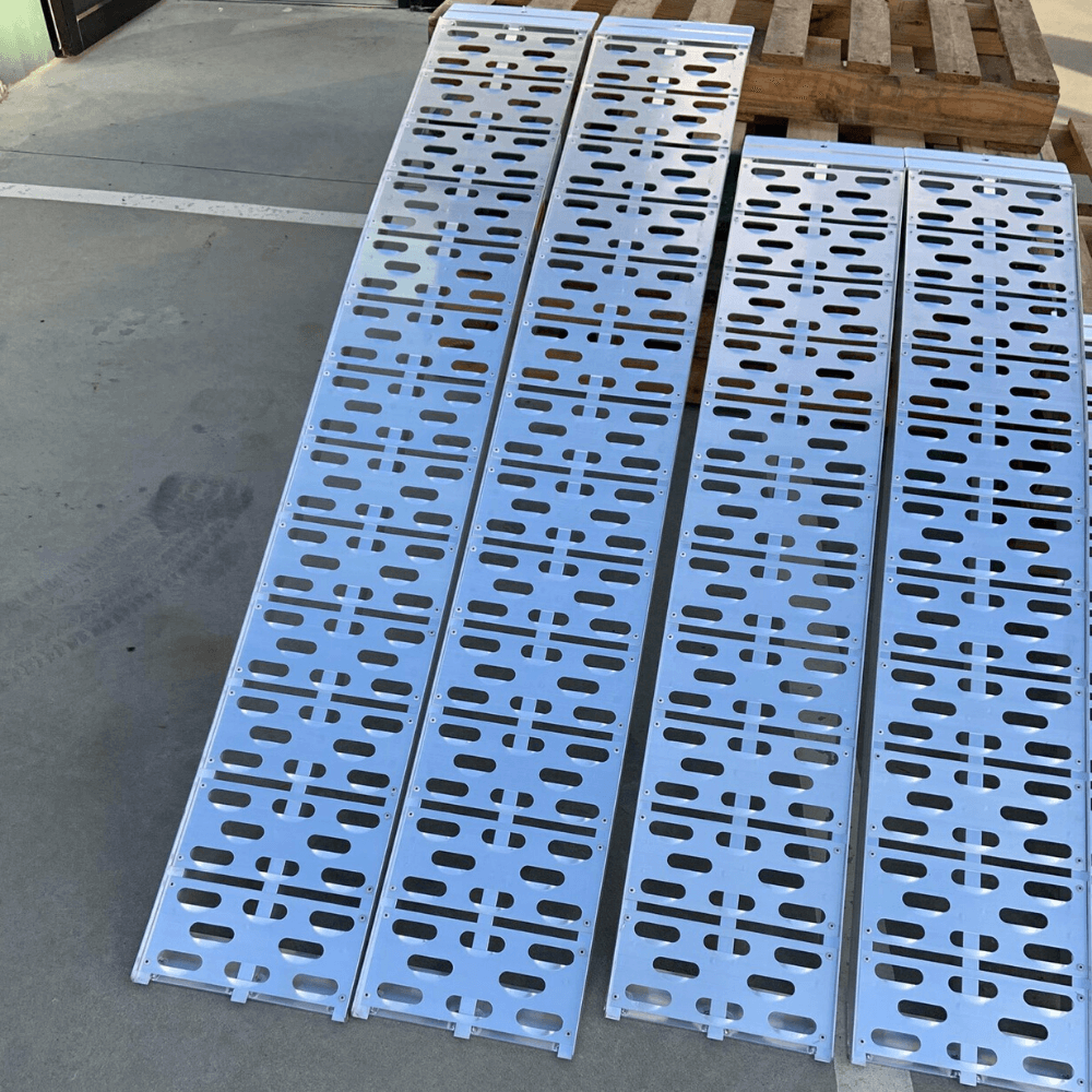 Two aluminium curved ramps in use on a grassy surface, propped up for loading.