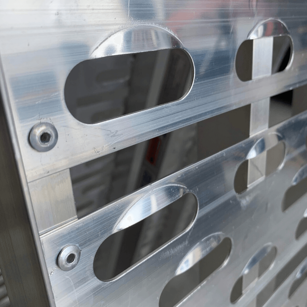 Close-up of perforated holes and grooves on an aluminium ramp surface.
