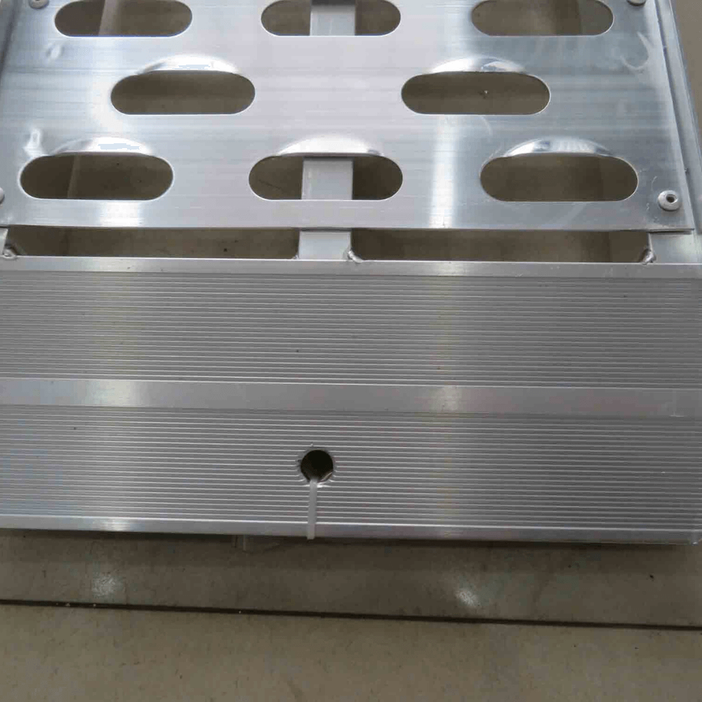 Close-up of perforated holes and grooves on an aluminium ramp surface.
