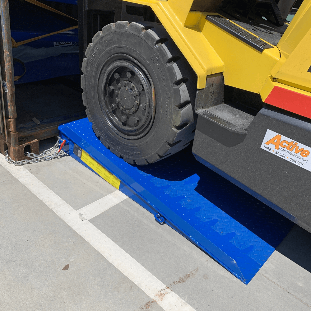 "Yellow Hyster 5.00 forklift driving up a bright blue loading ramp into a shipping container, with the ramp secured by a chain and safety label visible on the side."