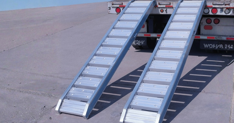 Two aluminium loading ramps attached to a flatbed truck, set up on pavement for loading heavy equipment.