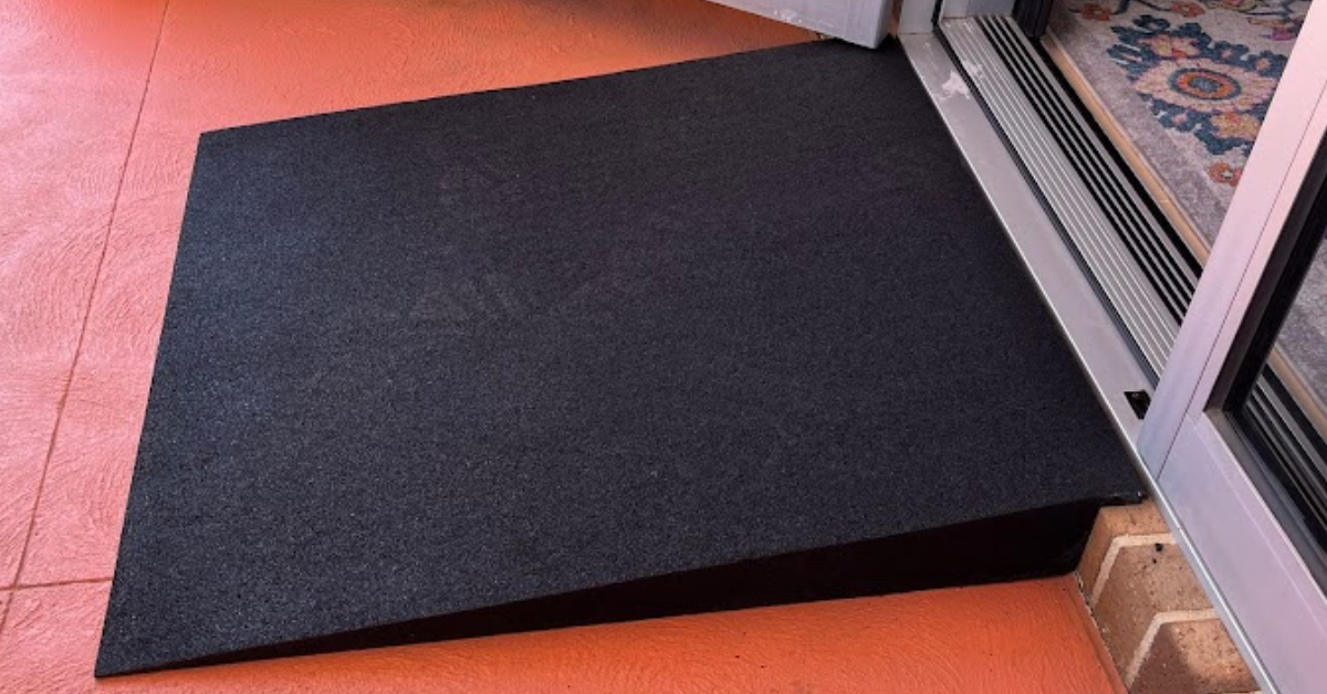 Black rubber threshold ramp on a floor next to a glass door