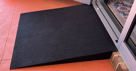 Black rubber threshold ramp on a floor next to a glass door