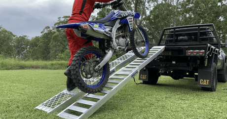 Man loading his motorcycle on a Whipps motorcycle ramp with side walk ramp installed to a ute
