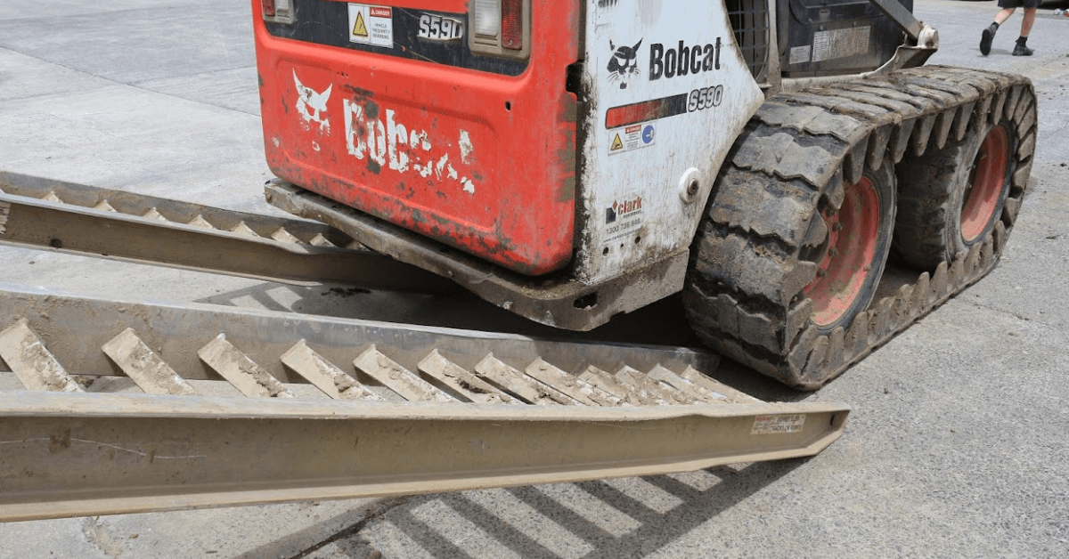 Photo of a skid steer loader about to load on a used pair of aluminium ramps 