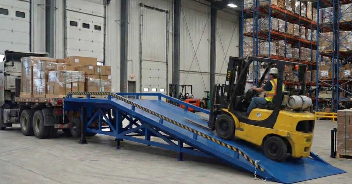 A yellow forklift drives up a blue yard ramp to access a loaded semi-truck inside a warehouse.