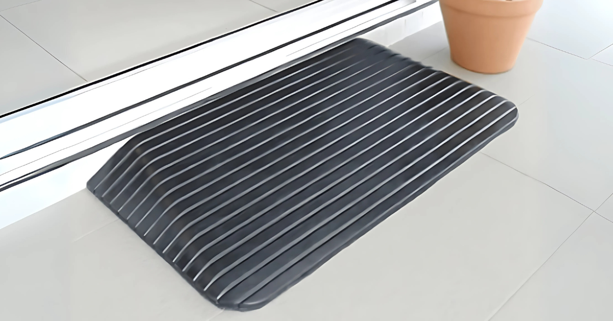 Black ribbed rubber threshold ramp placed at a sliding door entrance on a tiled floor, next to a terracotta plant pot.