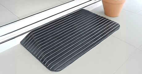 Black ribbed rubber threshold ramp placed at a sliding door entrance on a tiled floor, next to a terracotta plant pot.