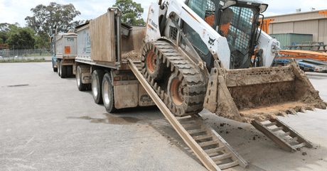 Bobcat skid steer loader travelling down loading ramps from truck