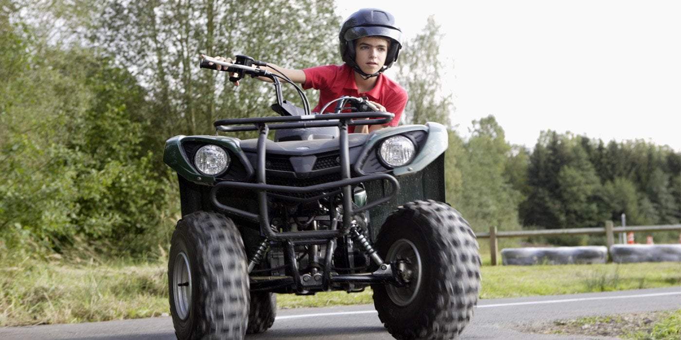 young man wearing helmet riding ATV on a road