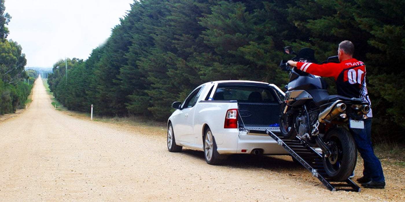 a man loading a motorcycle on a ute using a ramp