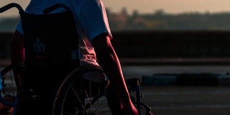 a man riding his wheelchair on a road during late afternoon