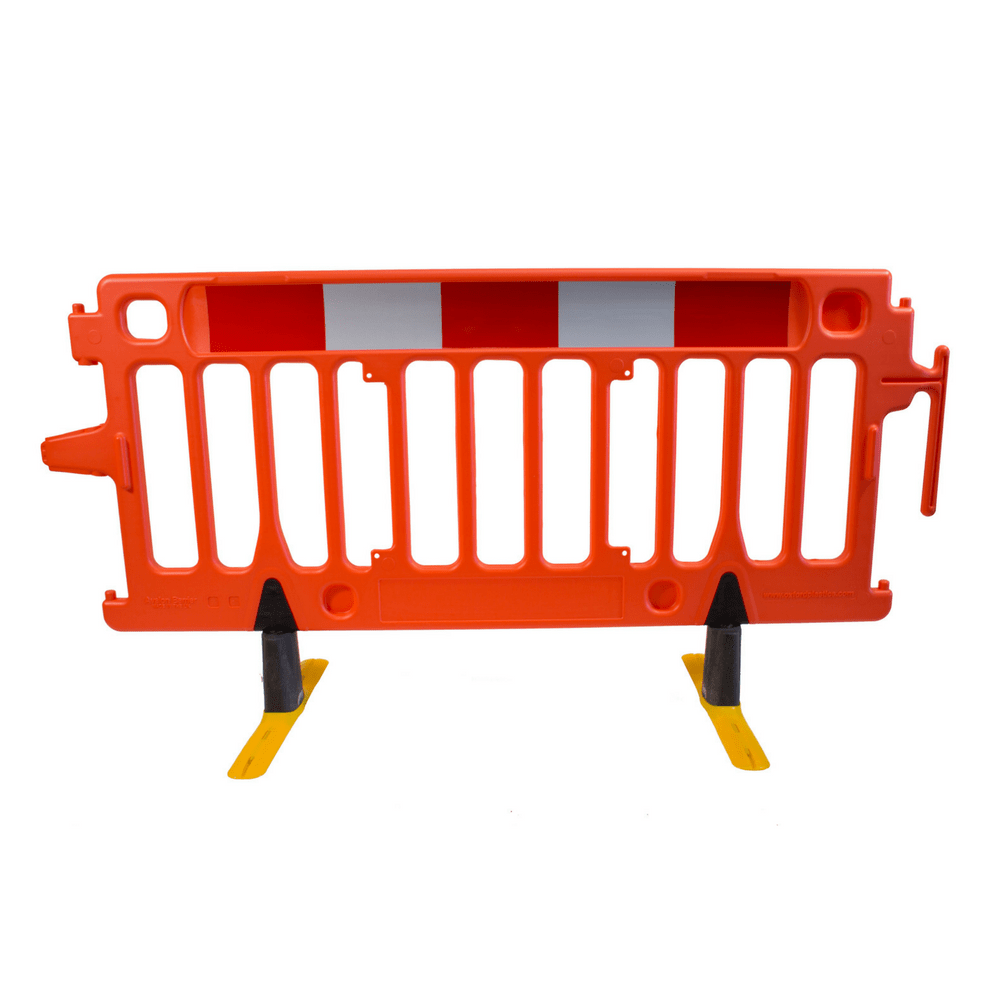 An orange plastic pedestrian barrier with reflective red and white strips, standing on yellow anti-trip swivel feet.