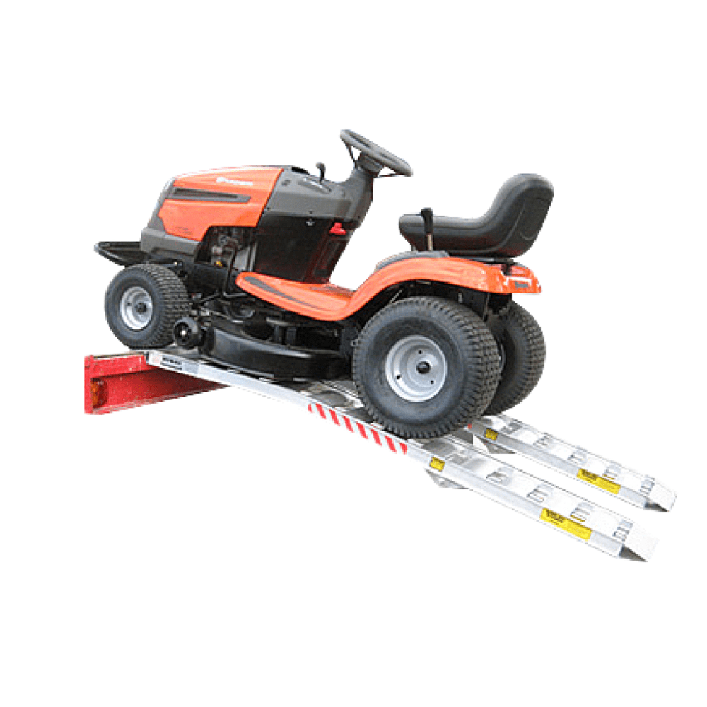 An orange riding lawn mower sits on two silver metal loading ramps attached to the back of a red vehicle.