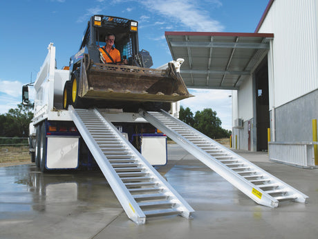 Skid steer driving up a pair of Sureweld PT Series aluminium loading ramps onto a truck