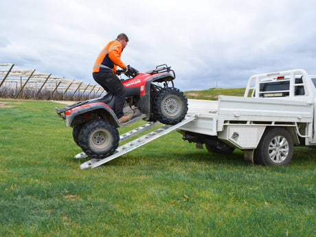 Rider driving a quad bike up a pair of Sureweld foldable aluminium loading ramps onto a ute tray
