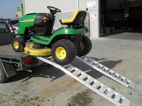 Ride-on mower on a pair of Sureweld curved foldable aluminium loading ramps at the back of a trailer