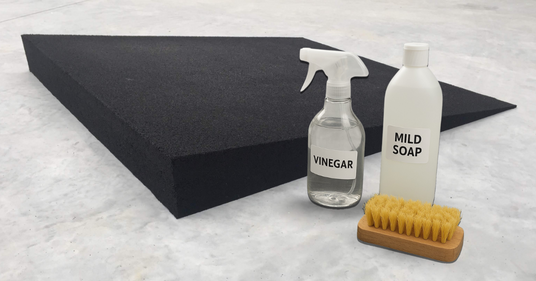 Cleaning supplies including vinegar, mild soap, a brush, and a black foam block on a white surface.
