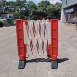 Red and white folding barrier on a concrete surface with trees and buildings in the background
