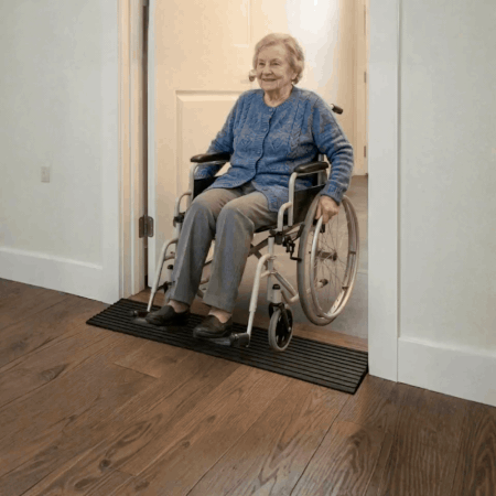 lifestyle image of a Heeve 900mm solid rubber door ramp, showing an elderly woman in a wheelchair using it.