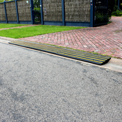 Black and yellow rubber kerb ramp installed at the edge of a residential driveway, aligned with a rolled-edge kerb for smooth vehicle access.