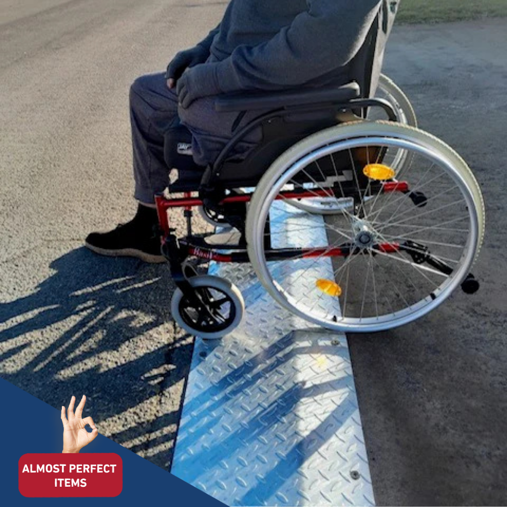 Elderly man in a wheelchair using a portable aluminium kerb ramp on a street, labelled as an “Almost Perfect Item.”