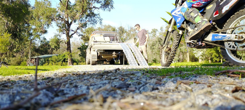 Person loading a motorcycle onto a trailer with a truck in the background
