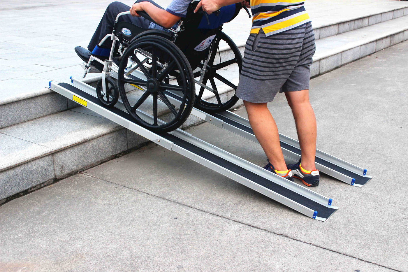 Pair of telescopic wheelchair ramps being used to push a wheelchair up concrete steps